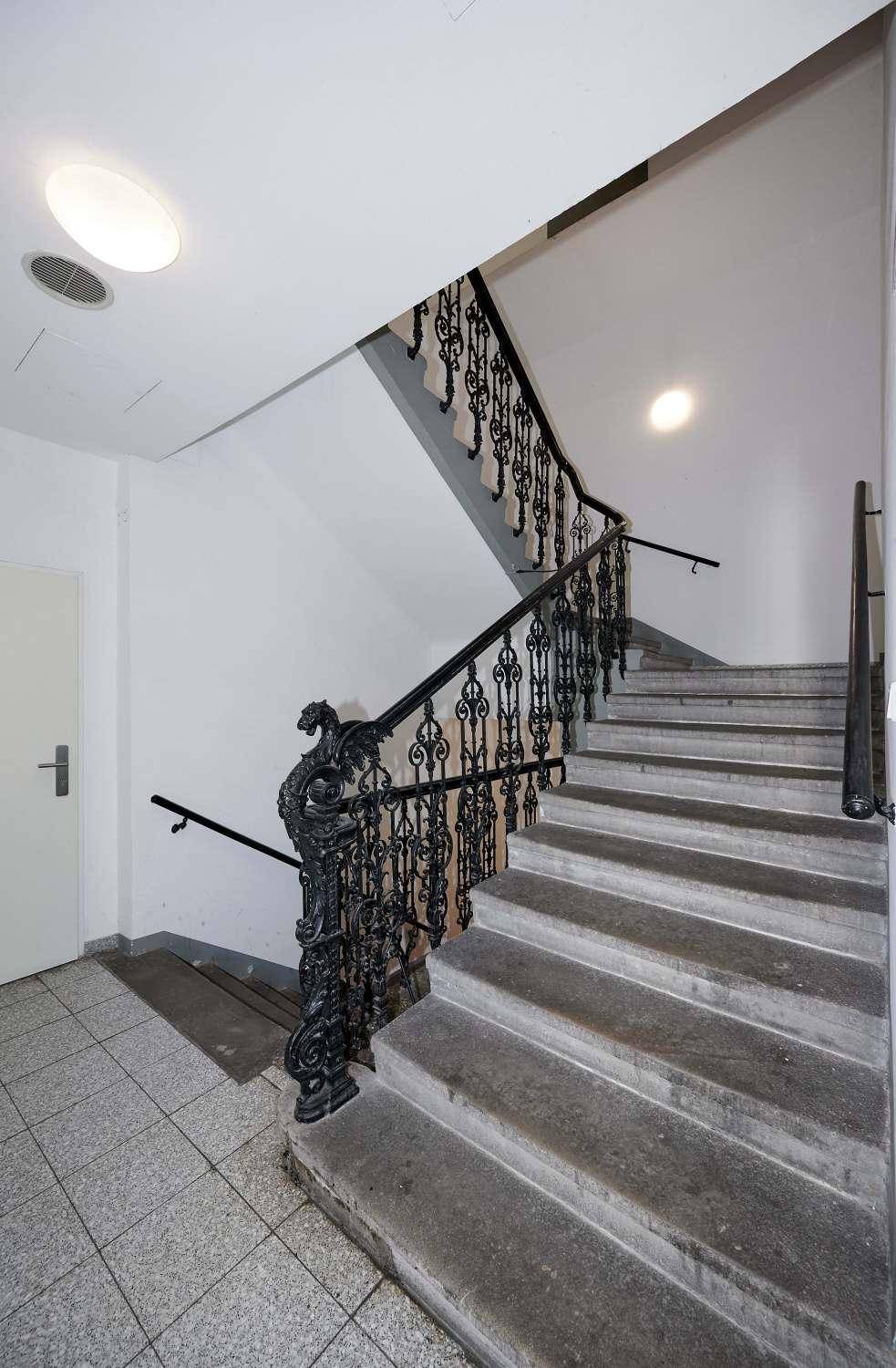 Breites Treppenhaus mit Steinstufen und kunstvollem schmiedeeisernem Geländer.