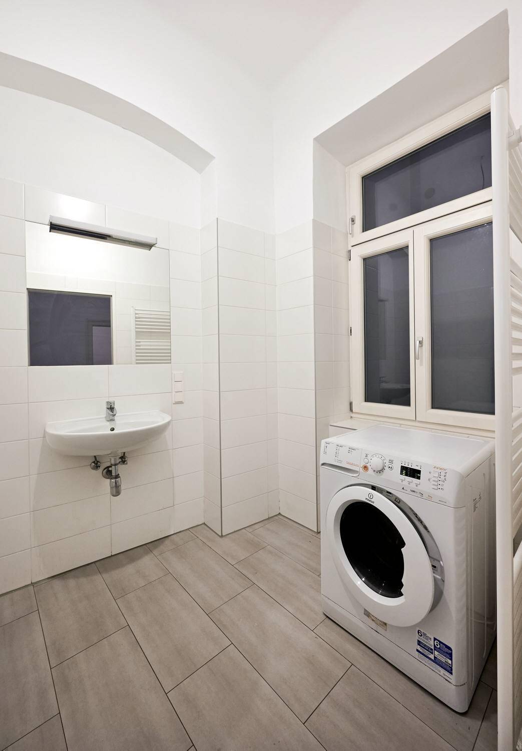 Helles Badezimmer mit Waschbecken, Waschmaschine und Fenster.