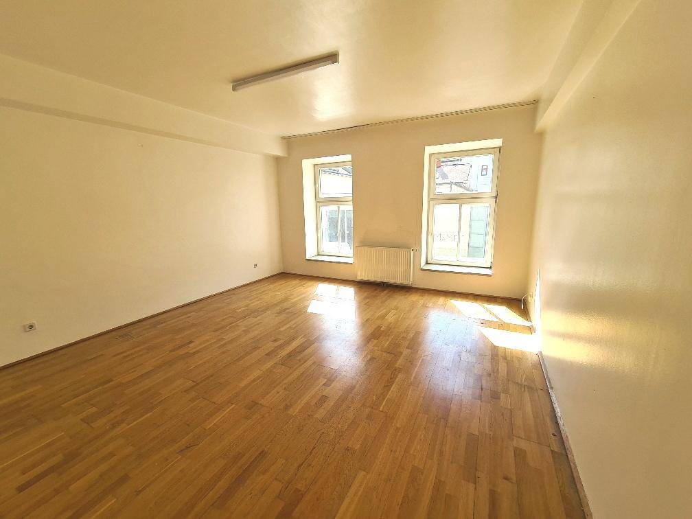 Geräumiges Zimmer mit hellem Parkettboden und großen Fenstern, ideal für verschiedene Nutzungen.