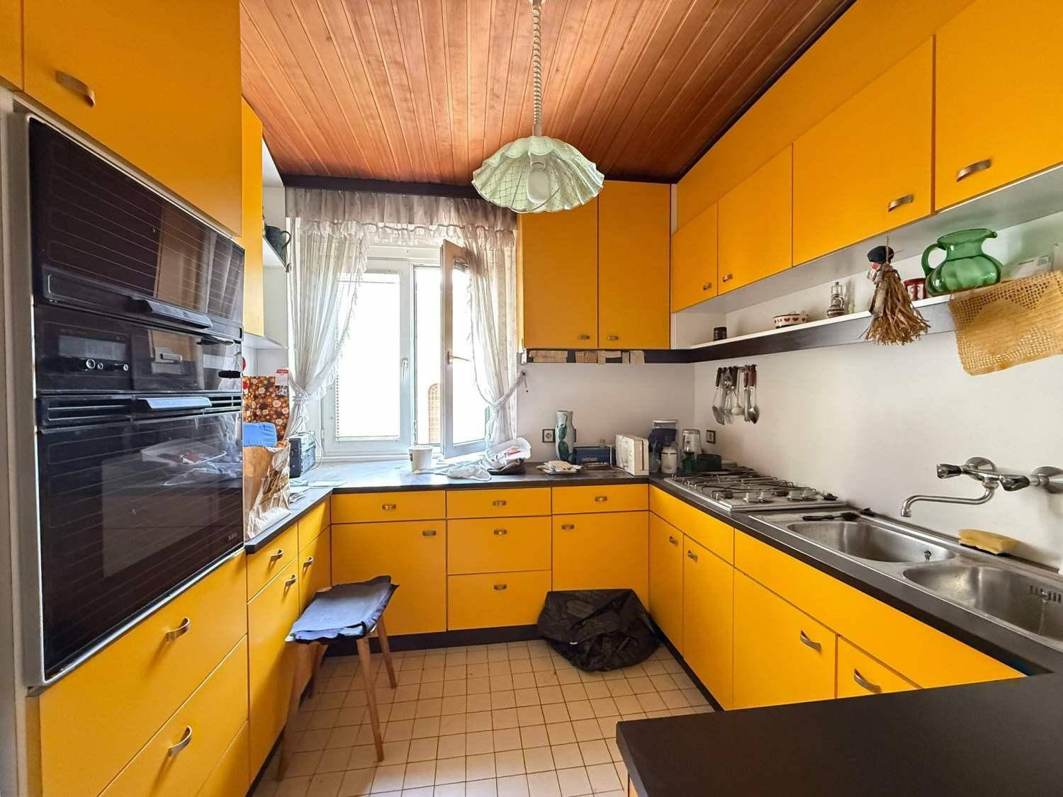 Helle Küche mit leuchtend gelben Schränken, schwarzen Arbeitsplatten und einer Holzdecke.