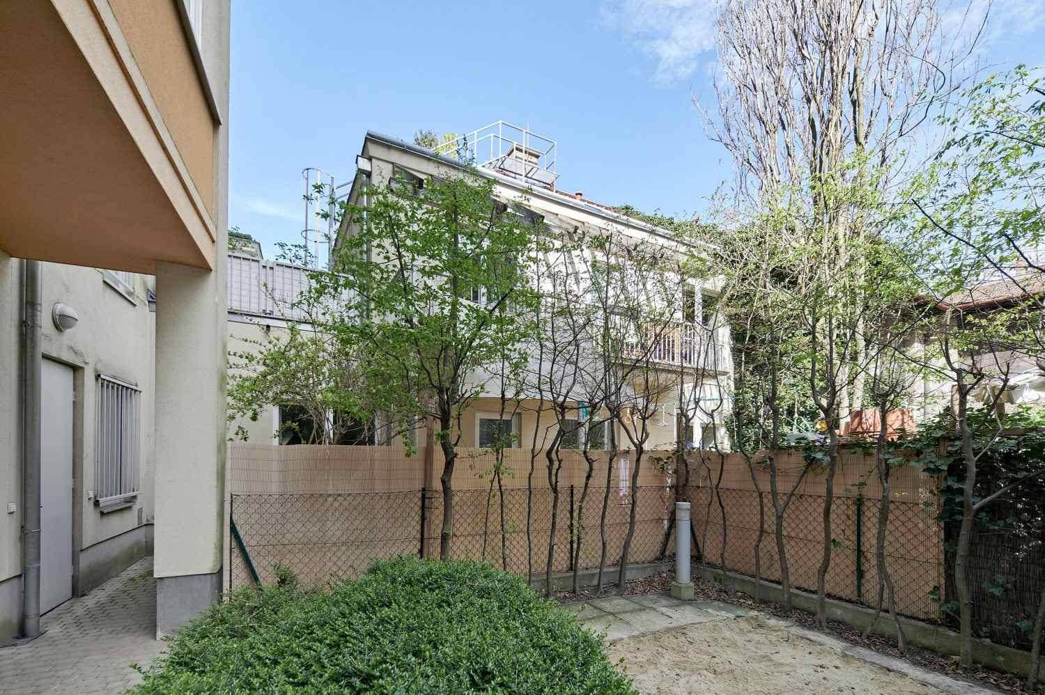 Hinterhof mit Bäumen, Zaun und Blick auf die Rückseite des Gebäudes.