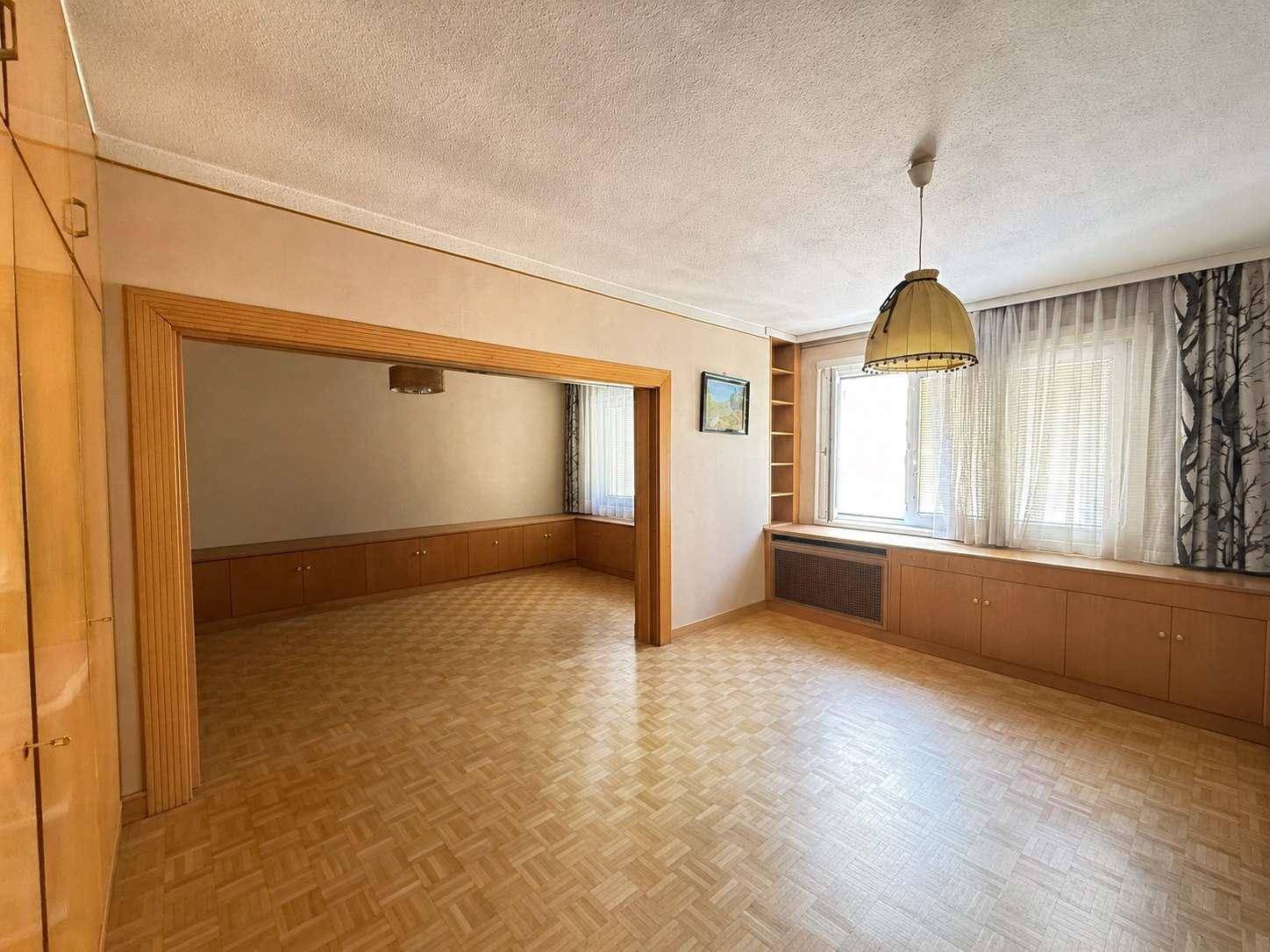 Leerer Raum mit Parkettboden, Einbauschränken entlang der Wände und einem Durchgang zu einem weiteren Zimmer.