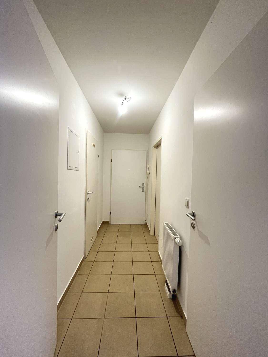 Langer, heller Flur mit Fliesenboden und weißen Wänden, der zu mehreren Türen führt.