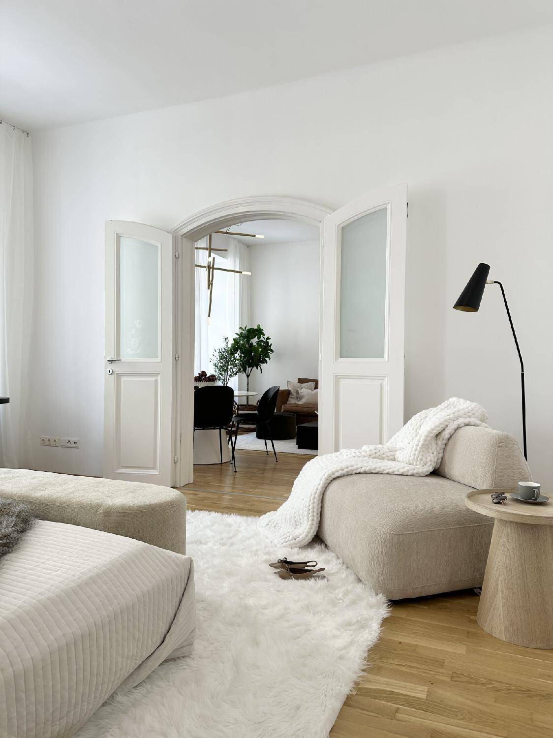 Gemütliches Schlafzimmer mit Blick durch eine elegante Doppeltür in den hellen Wohn- und Essbereich.