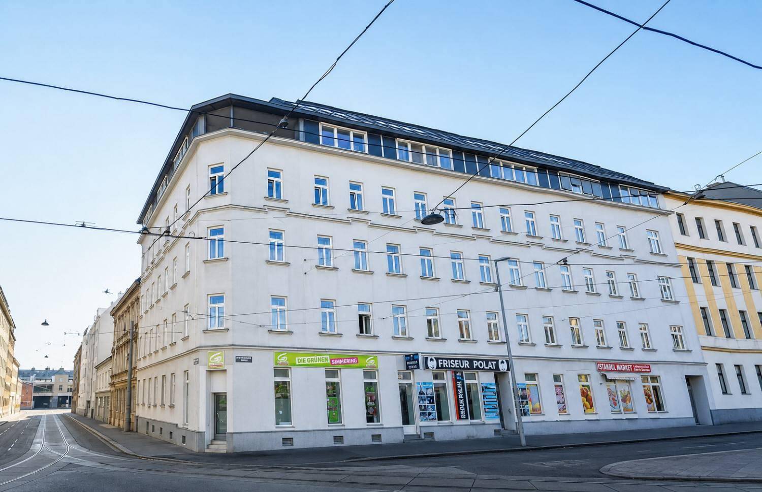 Eckgebäude mit moderner Fassade und Geschäften im Erdgeschoss an einer städtischen Straße.