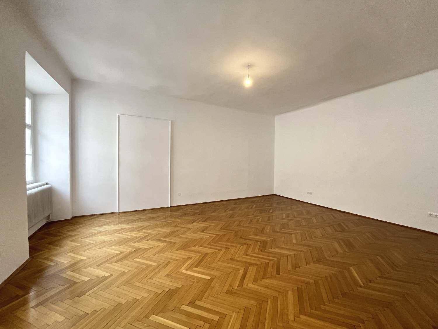 Helles, leeres Zimmer mit klassischem Fischgrätparkett und weiß gestrichenen Wänden.