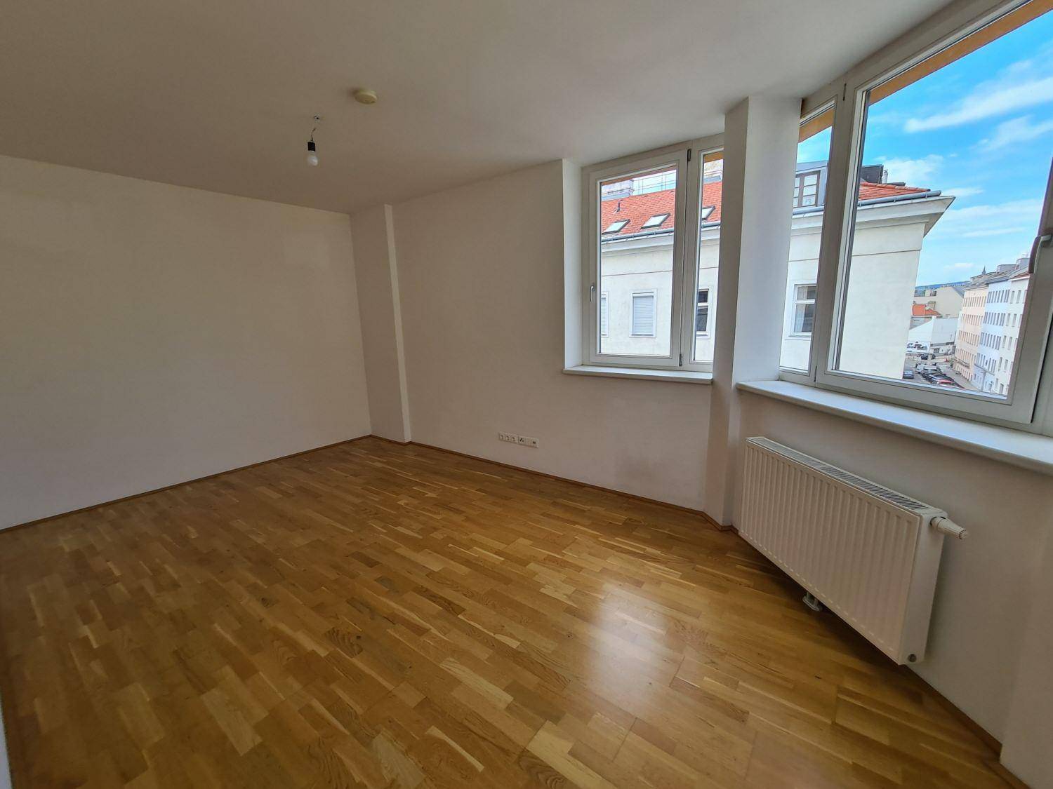 Helles Zimmer mit Parkettboden und großen Fenstern, die viel Tageslicht hereinlassen.