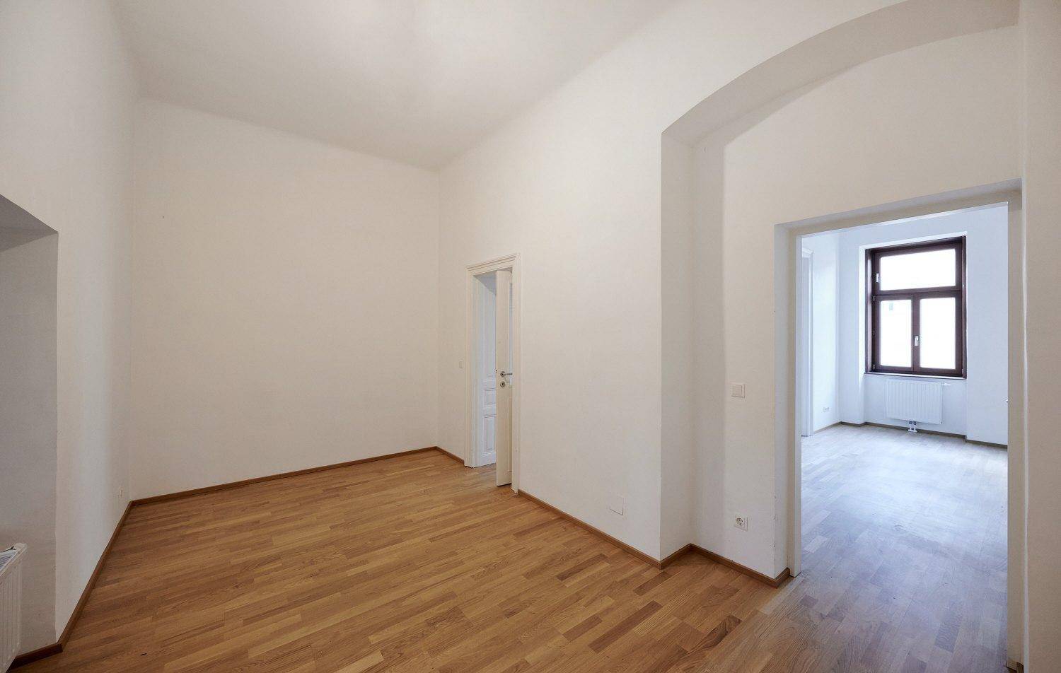 Leerer Raum mit Parkettboden und einem Durchgang zu einem weiteren Zimmer.