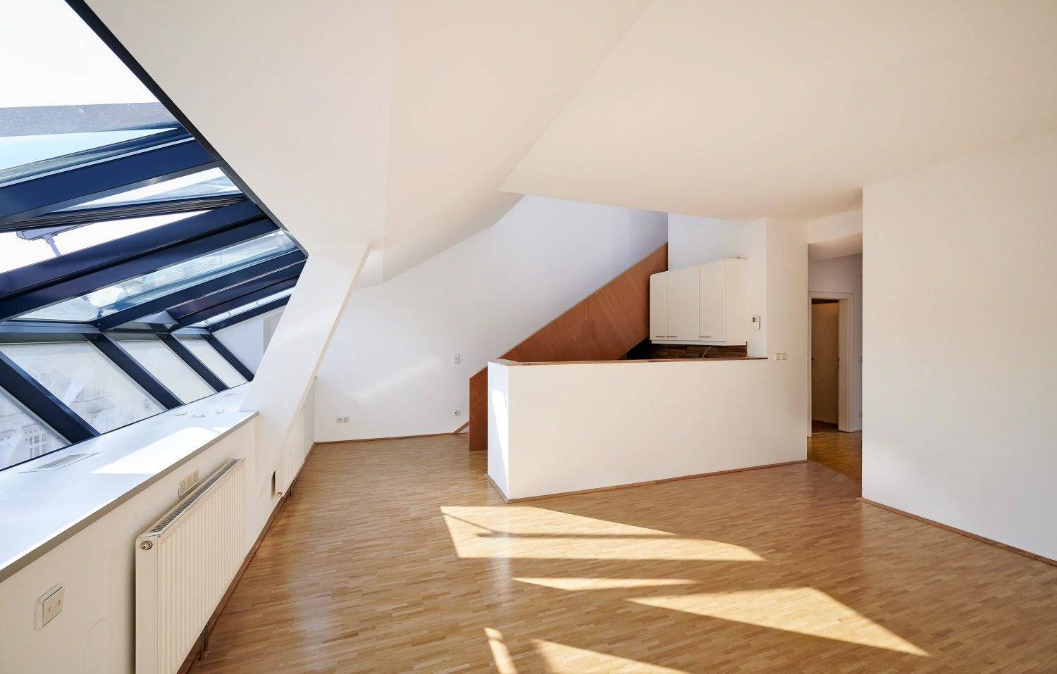 Offener Wohnbereich mit Küchenzeile, Holzboden und viel natürlichem Licht durch Dachfenster.