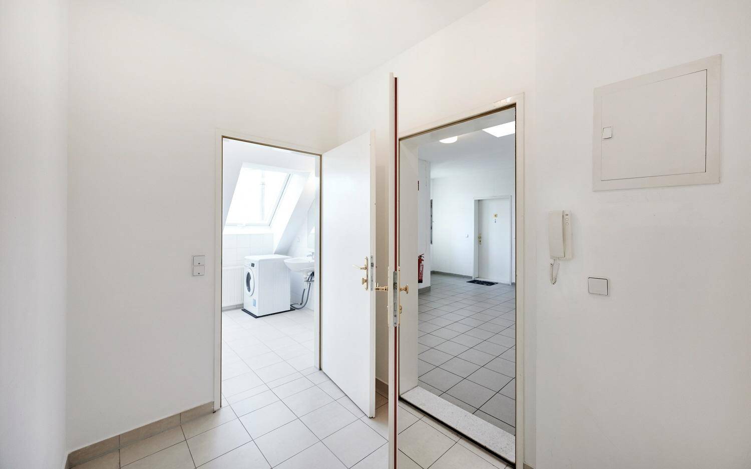 Eingangsbereich mit Fliesenboden und Zugang zu weiteren Räumen, inklusive Badezimmer mit Waschmaschine.