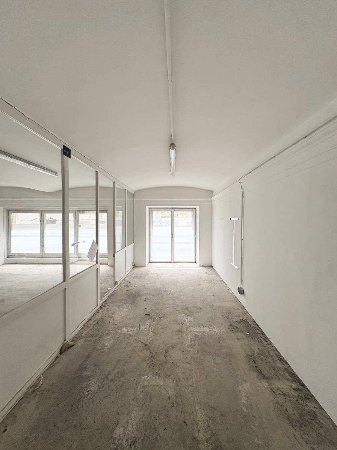 Langer Flurbereich im Gewerberaum mit Glasabtrennungen und einem großen Fenster am Ende, heller Betonboden.