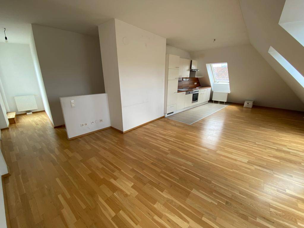 Geräumiger Wohnbereich mit offener Küche, Parkettboden und Dachschrägen, hell und einladend.