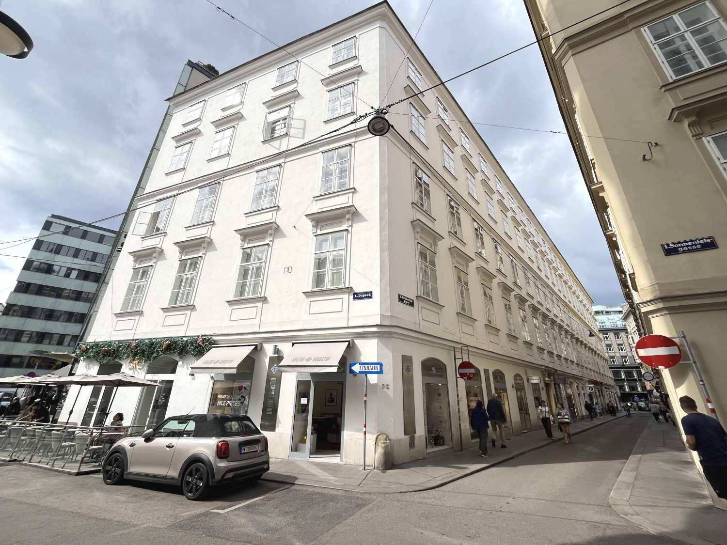 Historisches Eckgebäude in der Stadt mit Geschäften im Erdgeschoss und vielen Fenstern.