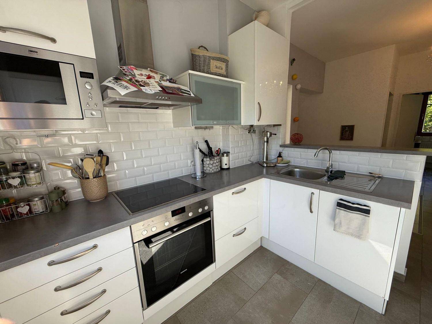 Moderne Küche mit weißen Hochglanzfronten, Induktionskochfeld und Fliesenrückwand.