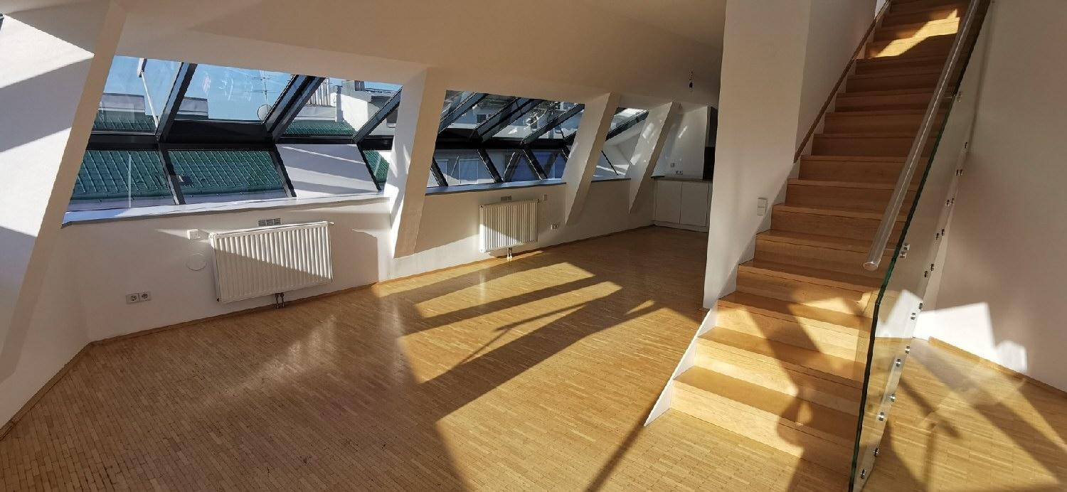 Helles Wohnzimmer mit Holzparkett und moderner Treppe, durchflutet von natürlichem Licht durch große Fenster.