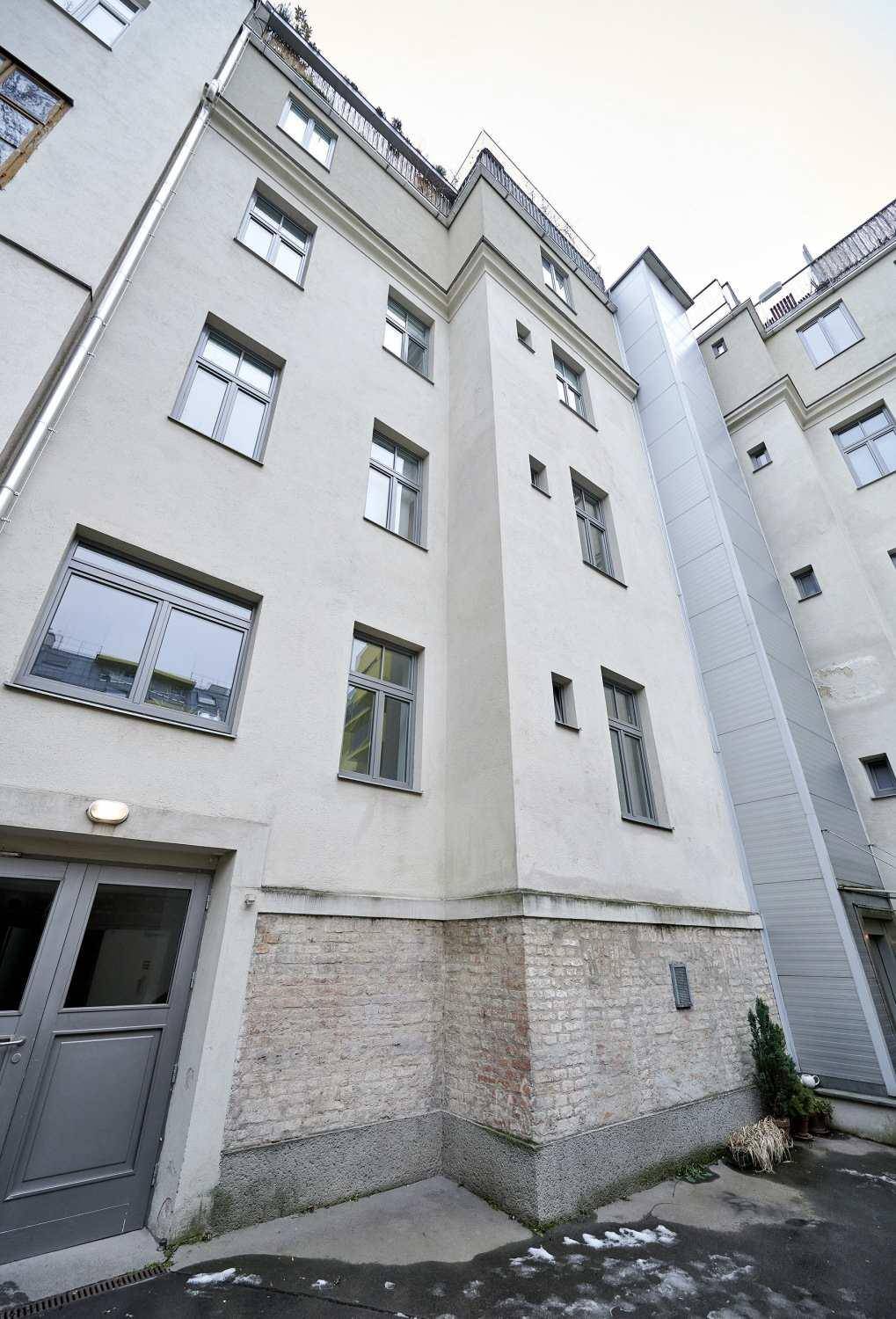 Innenhoffassade eines Mehrfamilienhauses mit verschiedenen Fenstern und einem Aufzugsschacht.