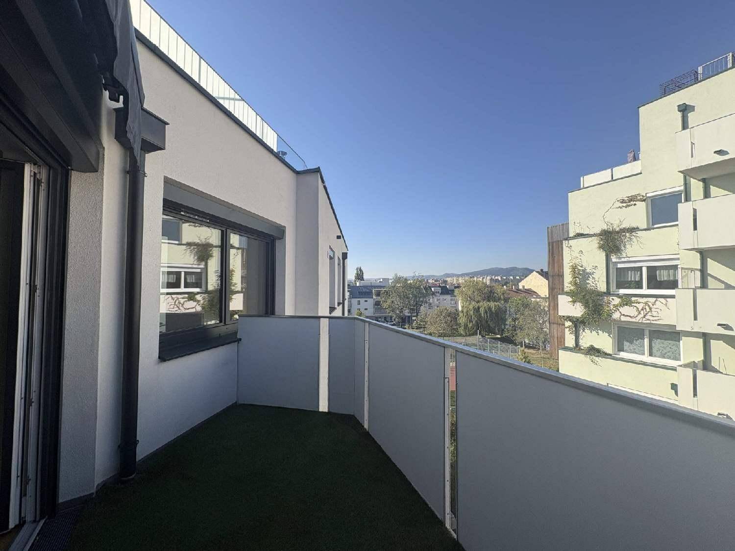 Balkon mit Kunstrasen und Blick auf die umliegende Bebauung und entfernte Hügel.