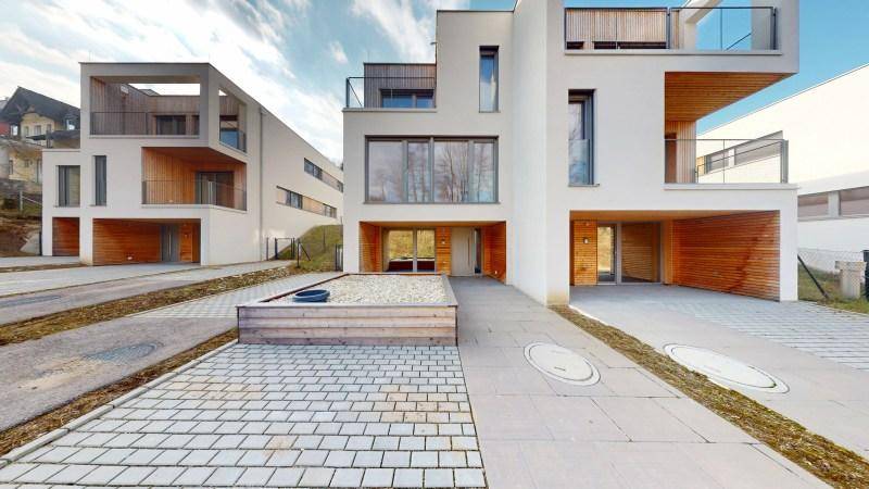 Moderne Reihenhäuser mit weißer Fassade, Holzverkleidung und gepflasterten Zufahrten.