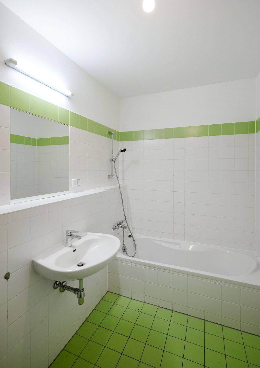 Funktionales Badezimmer mit Badewanne, Waschbecken und grünen Akzentfliesen an Wänden und Boden.