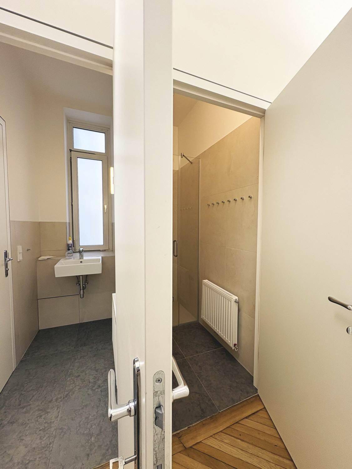 Modernes Badezimmer mit Dusche, Waschbecken und Fenster, ausgestattet mit hellen Fliesen.