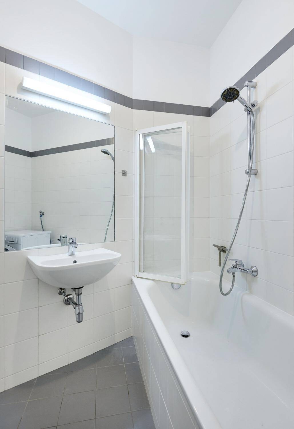 Funktionales Badezimmer mit Badewanne, Duschfunktion und weißem Fliesenbelag.