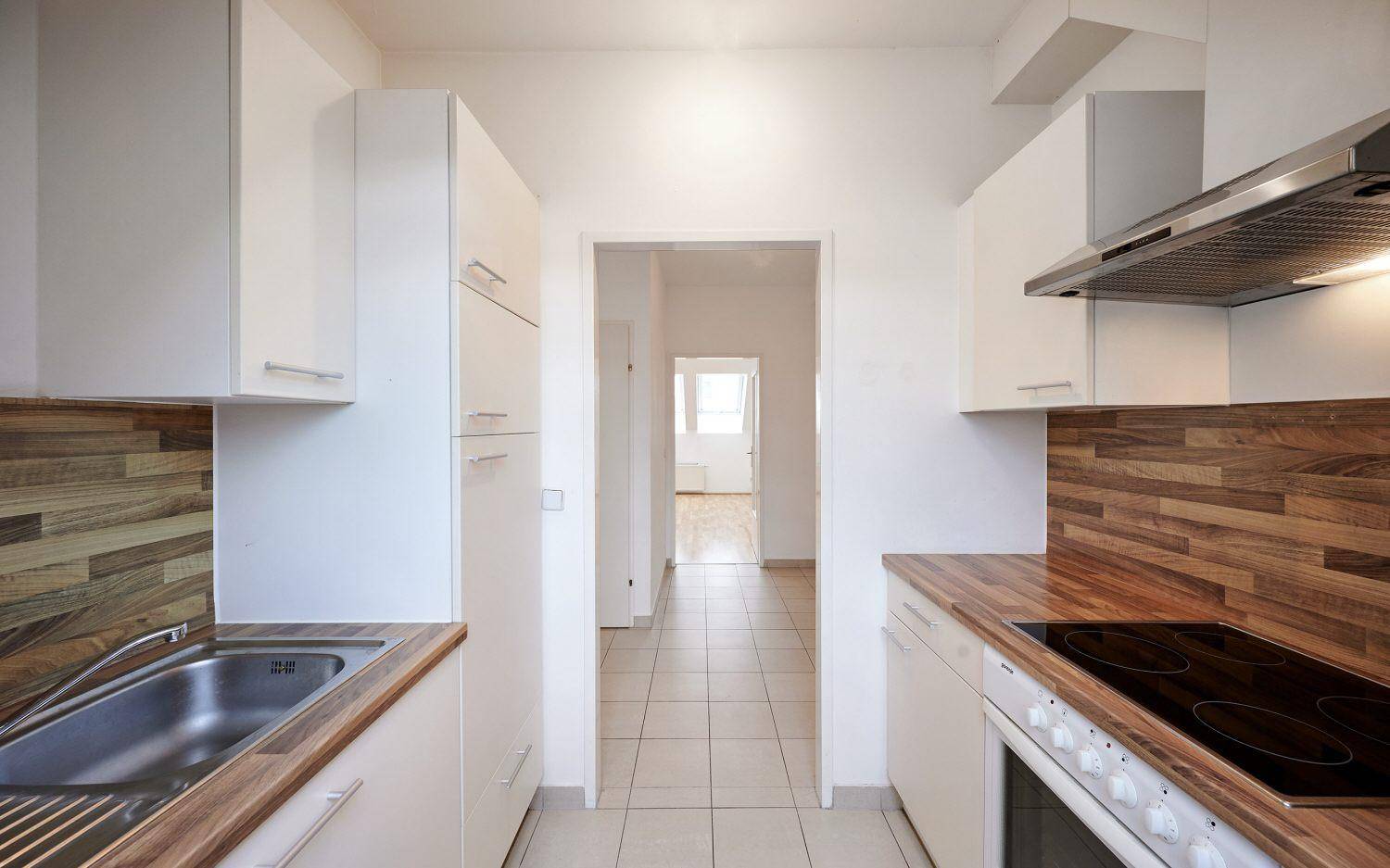 Funktionale Küche mit weißen Schränken, Holzarbeitsplatten und Blick in den gefliesten Flur.