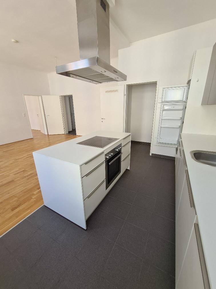 Offene Küche mit Kochinsel, Backofen und Dunstabzugshaube in hellem, modernem Design.