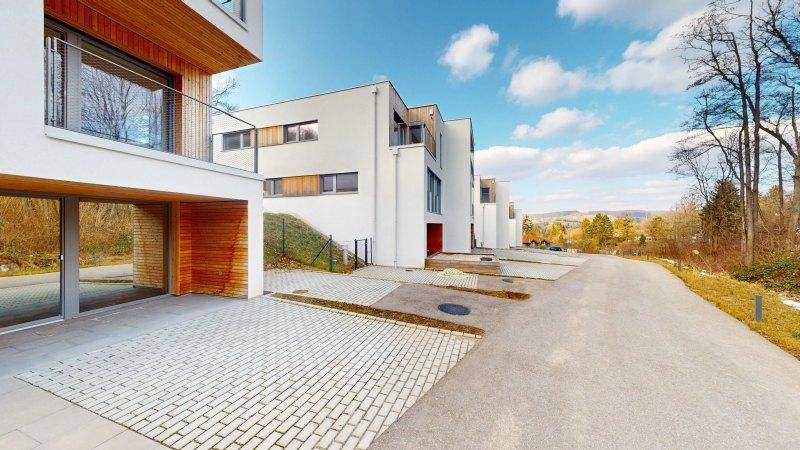 Reihe moderner Häuser mit weißer Fassade und Holzdetails entlang einer Zufahrtsstraße.