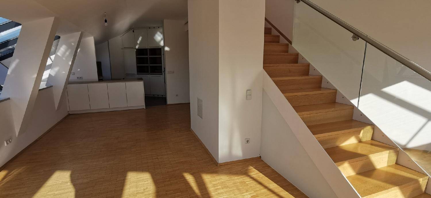 Offener Wohnbereich mit Holzparkett und Treppe, im Hintergrund ist ein Teil der Küche sichtbar.