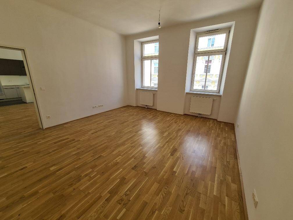 Geräumiger, heller Raum mit Holzboden und zwei Fenstern, bereit zur individuellen Gestaltung.