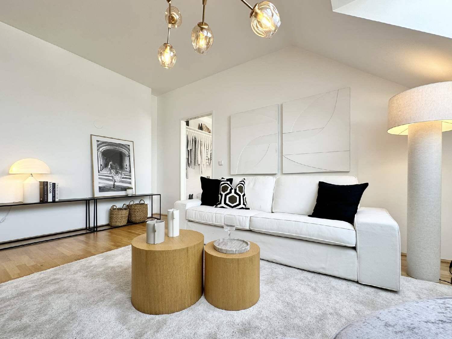 Heller Wohnbereich mit weißem Sofa, modernen Couchtischen und stilvoller Stehlampe.