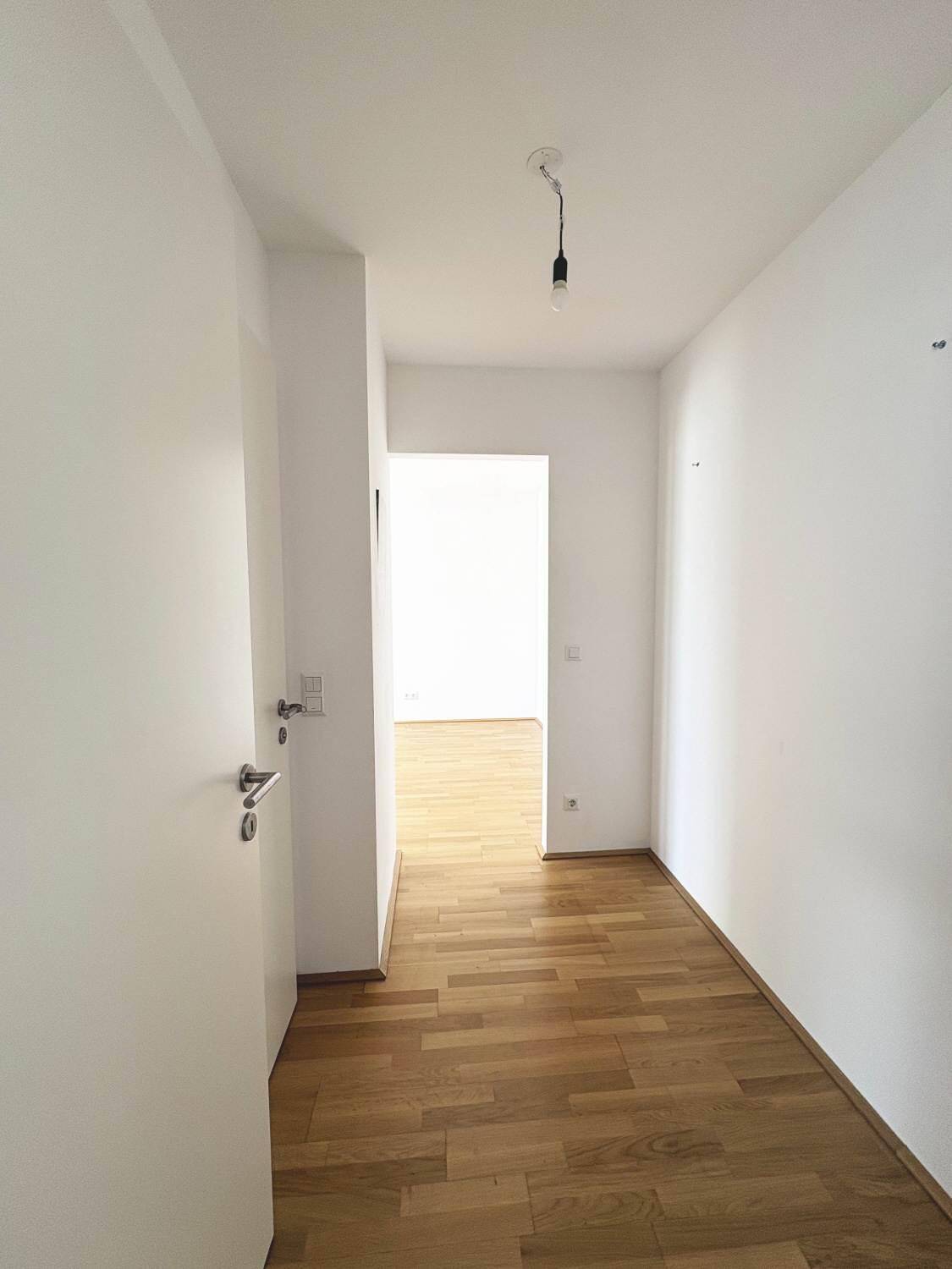 Heller Flur mit Holzboden und weißen Türen, der zu weiteren Räumen führt.