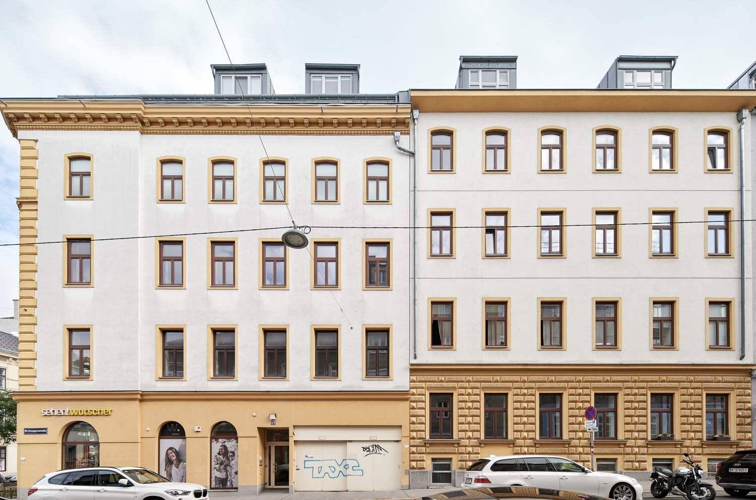 Ansicht von zwei angrenzenden Mehrfamilienhäusern mit mehreren Stockwerken und Dachgauben an einer Straße.