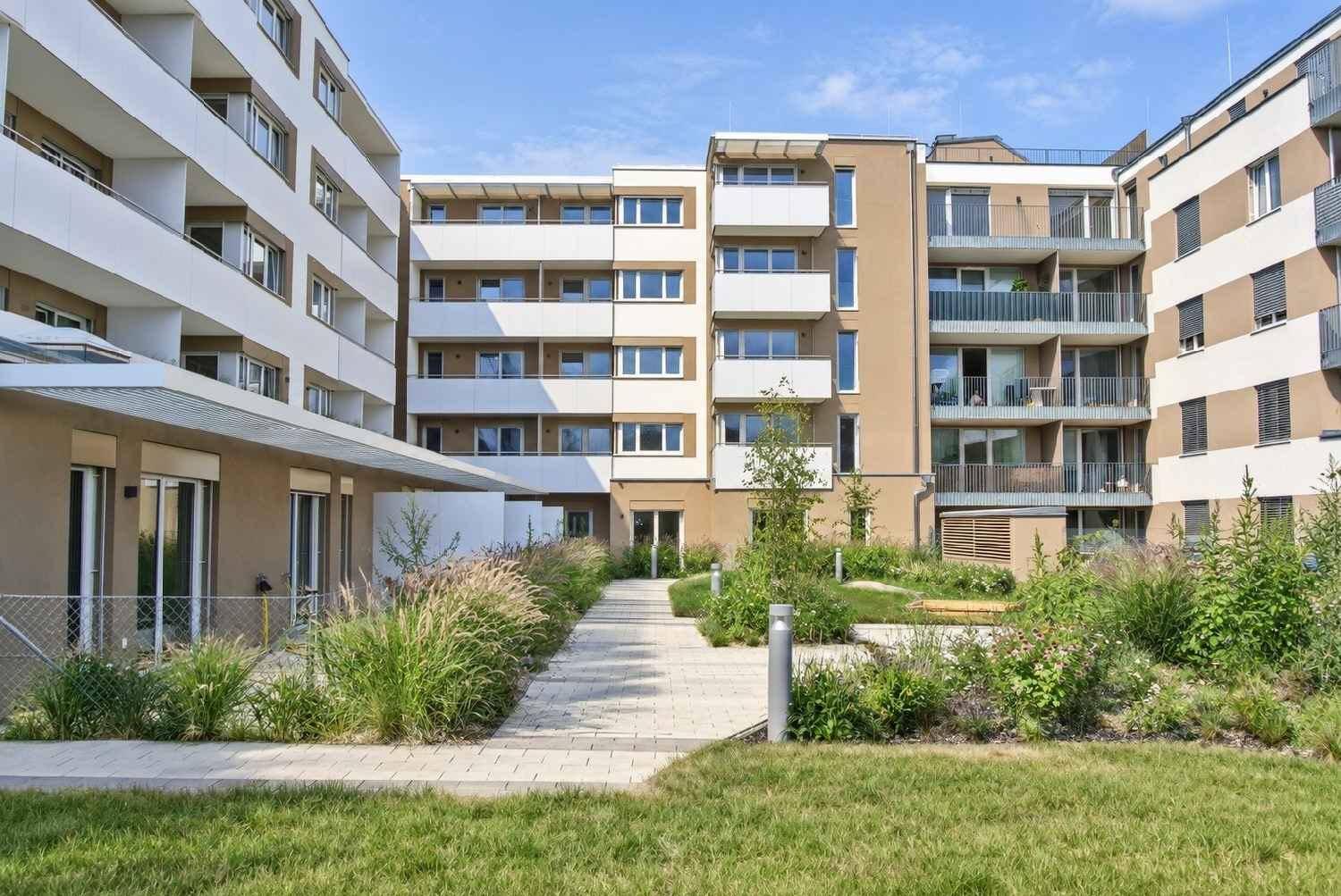 Begrünter Innenhof einer modernen Wohnanlage mit Wegen und Bepflanzung.