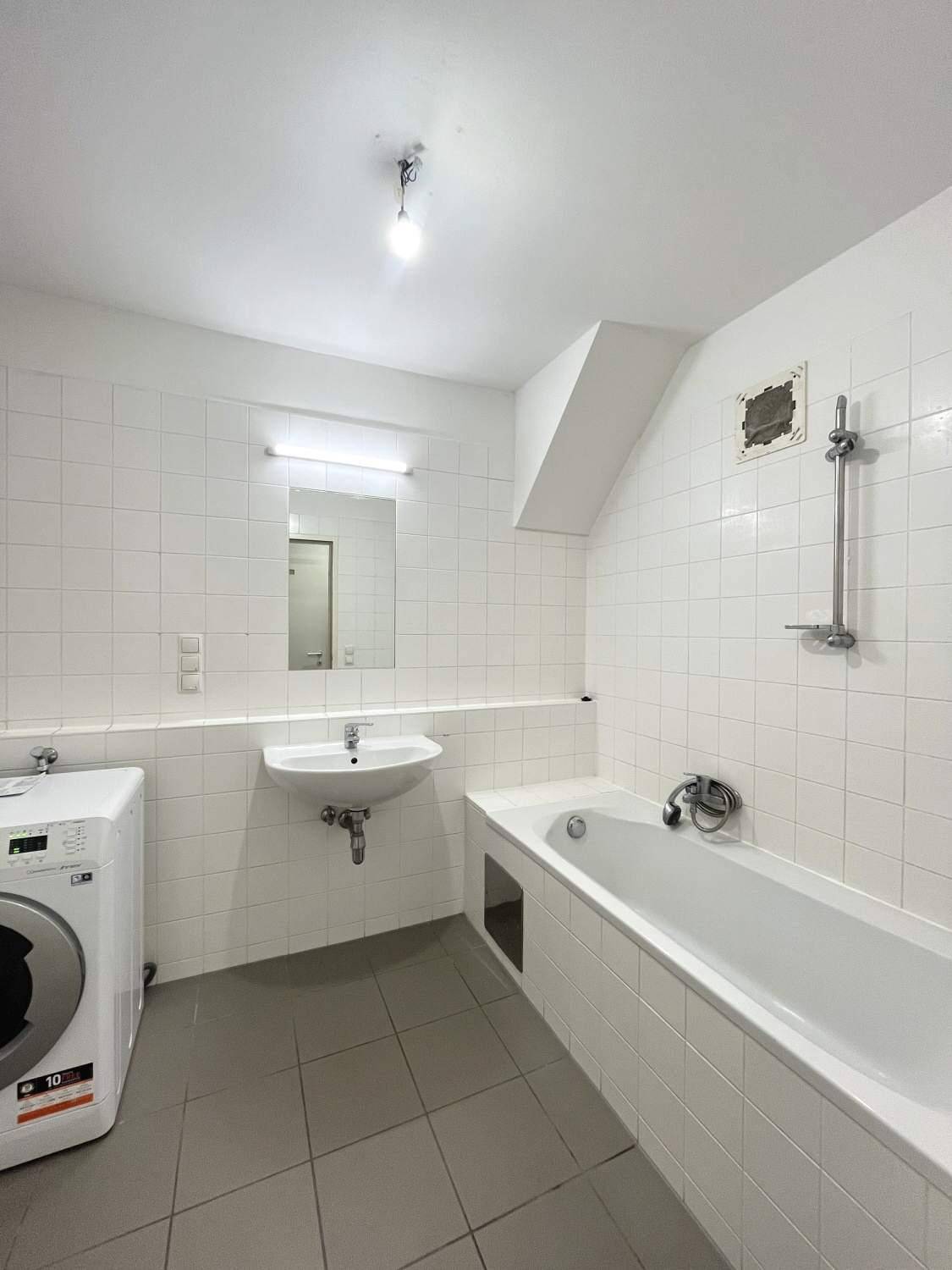 Badezimmer mit Badewanne, Waschbecken und Waschmaschine, komplett gefliest in Weiß.