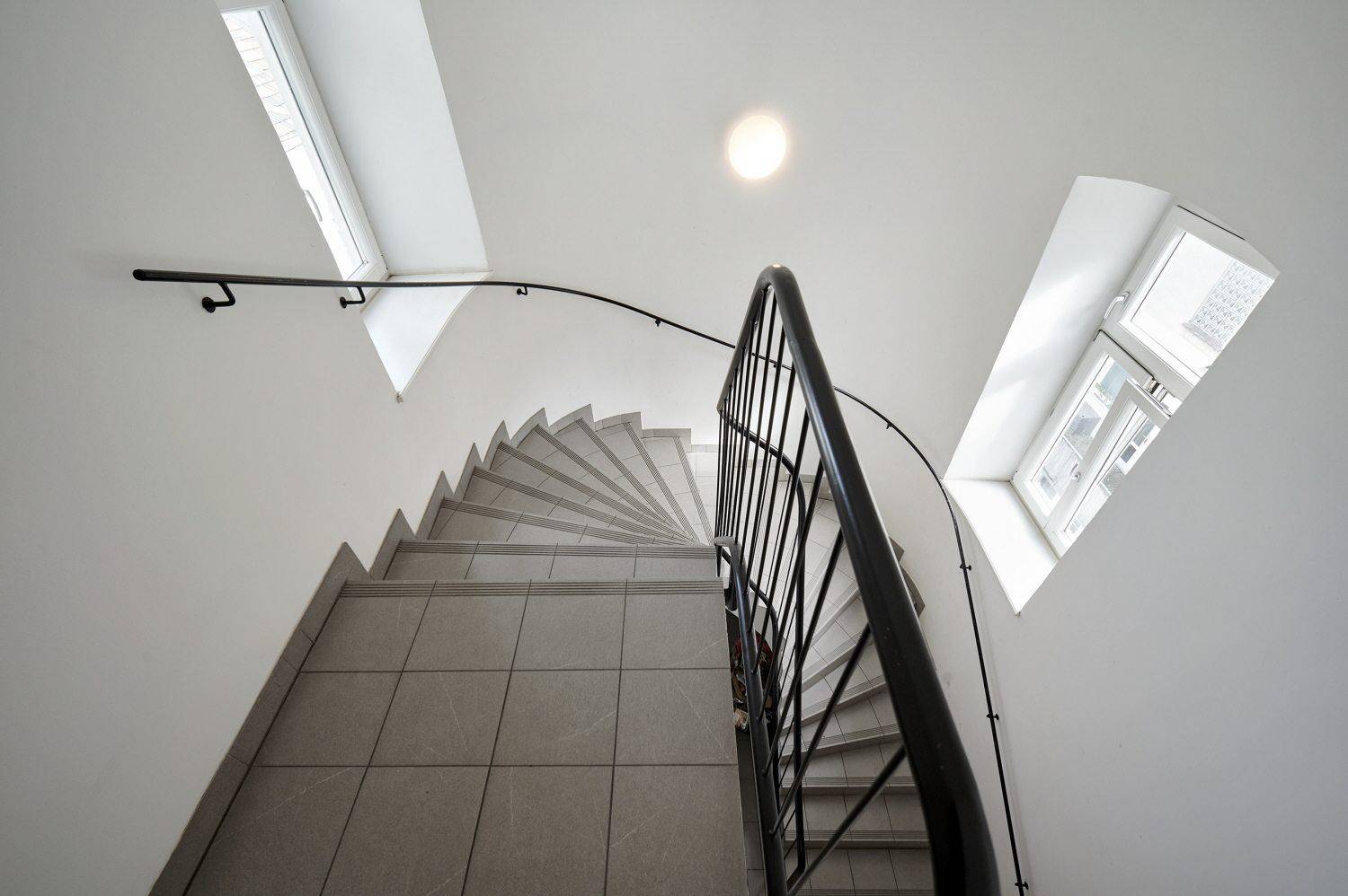 Modernes Treppenhaus mit gefliesten Stufen, elegantem Geländer und natürlichem Licht durch Dachfenster.