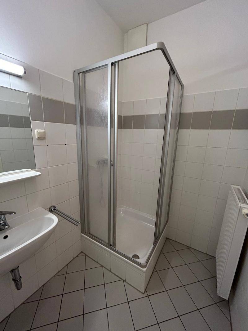 Badezimmer mit Duschkabine, Waschbecken und Fliesen in Weiß und Grau.