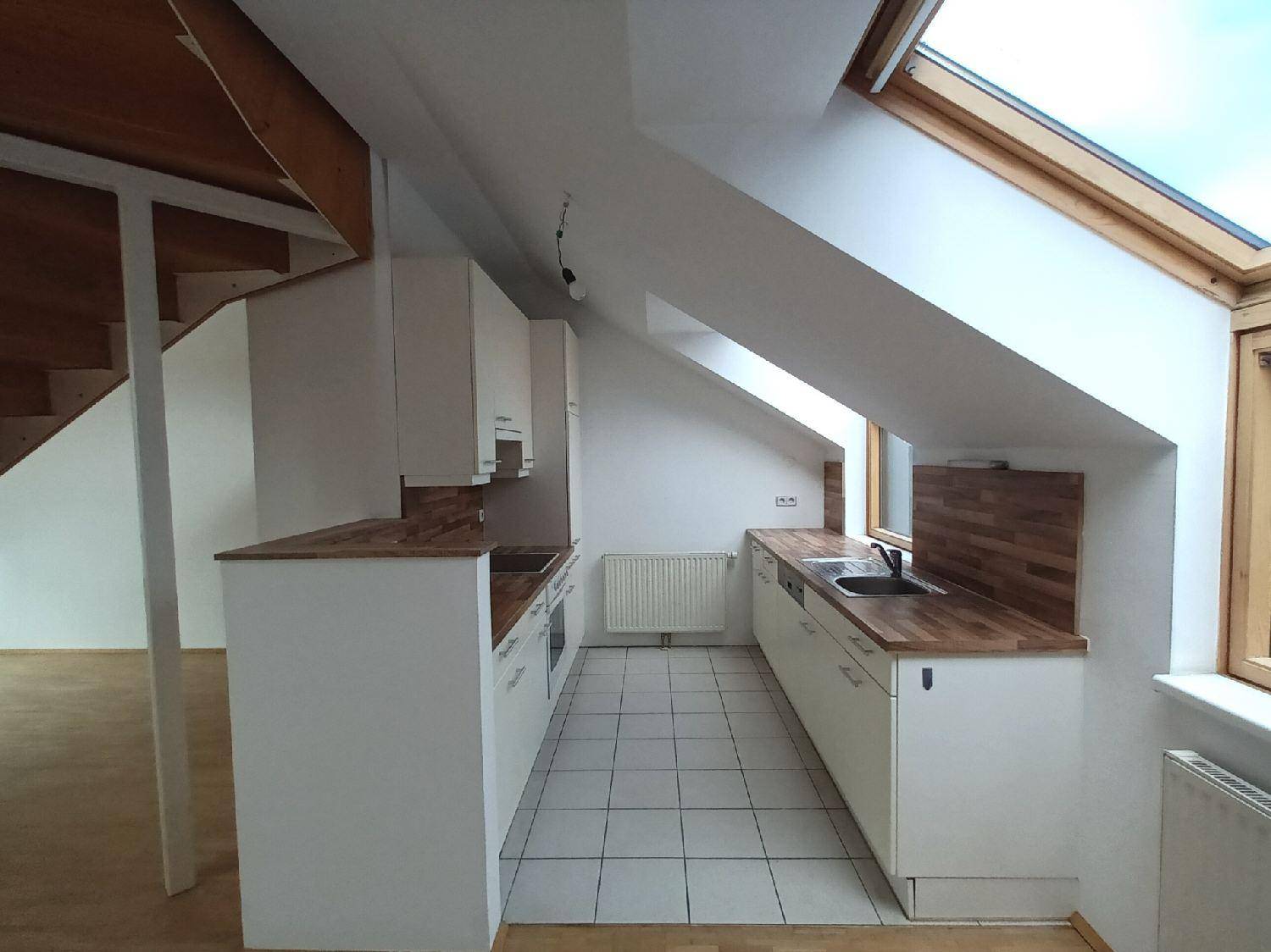 Kleine Küche im Dachgeschoss mit weißen Schränken, Holz-Arbeitsplatten und Fliesenboden unter schräger Decke.