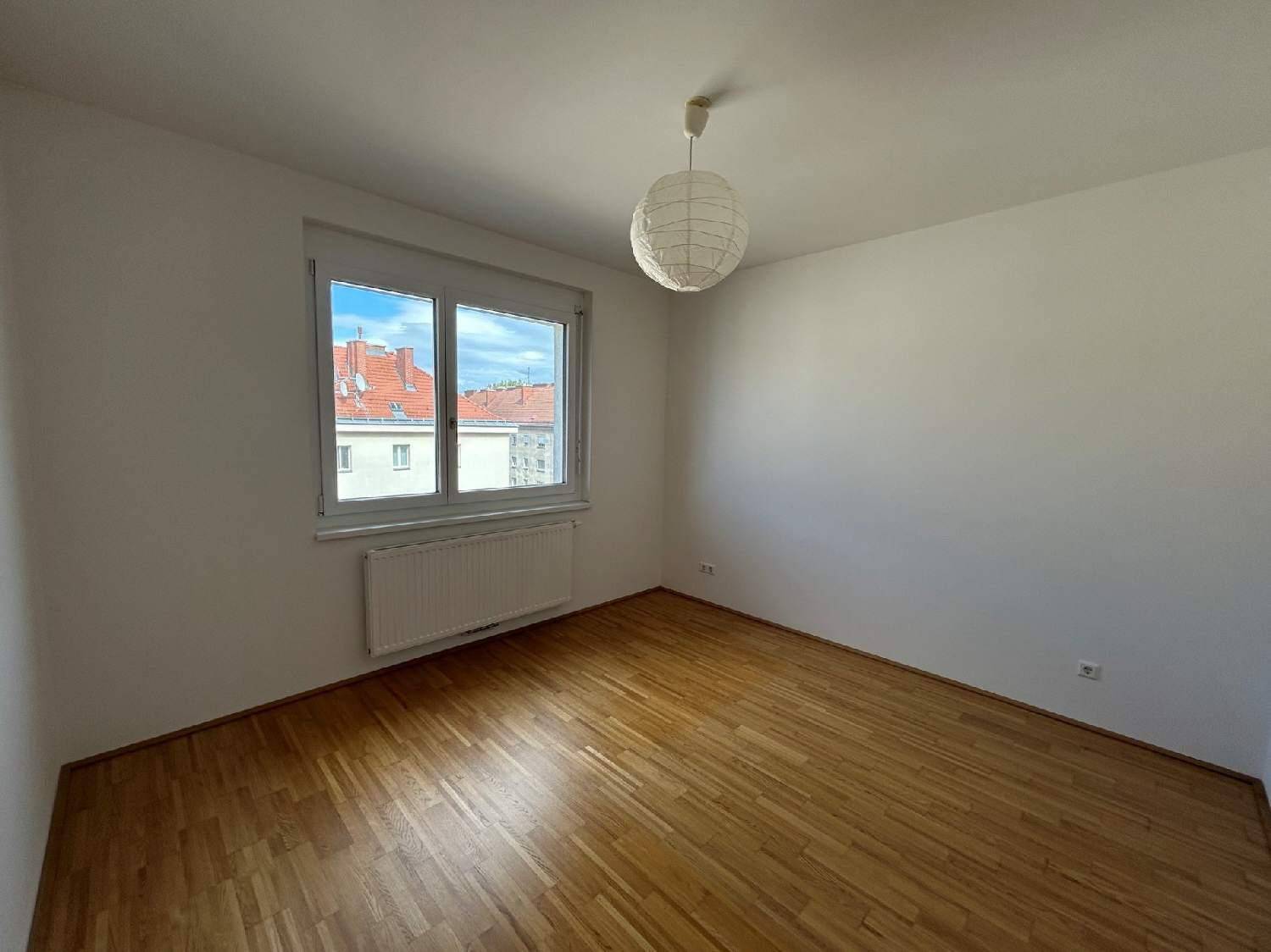 Helles Schlafzimmer mit Parkettboden, großem Fenster und Blick auf die umliegenden Dächer.