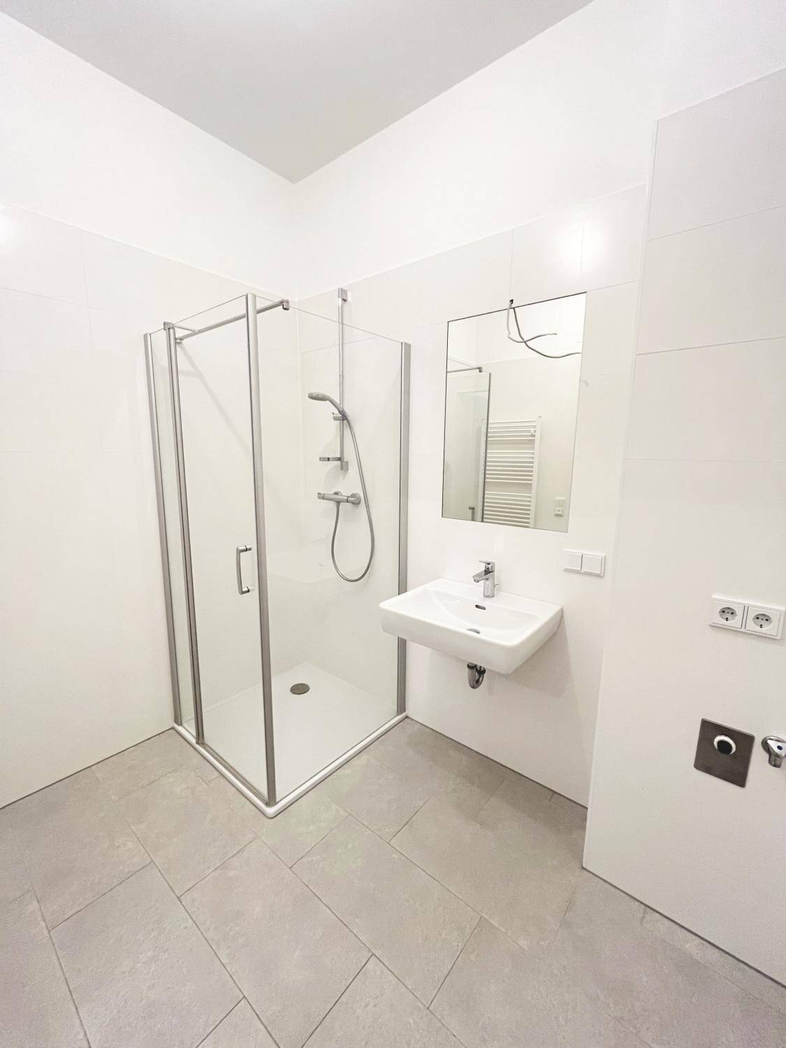 Modernes Badezimmer mit Duschkabine, Waschbecken und beheiztem Handtuchhalter.