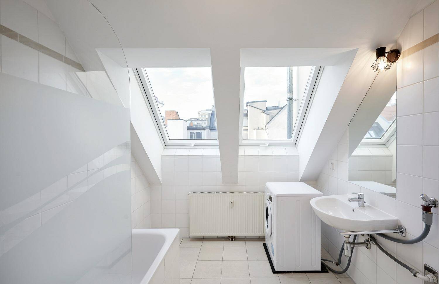 Geräumiges Badezimmer mit Badewanne, Waschbecken, Waschmaschine und viel Tageslicht durch Dachfenster.