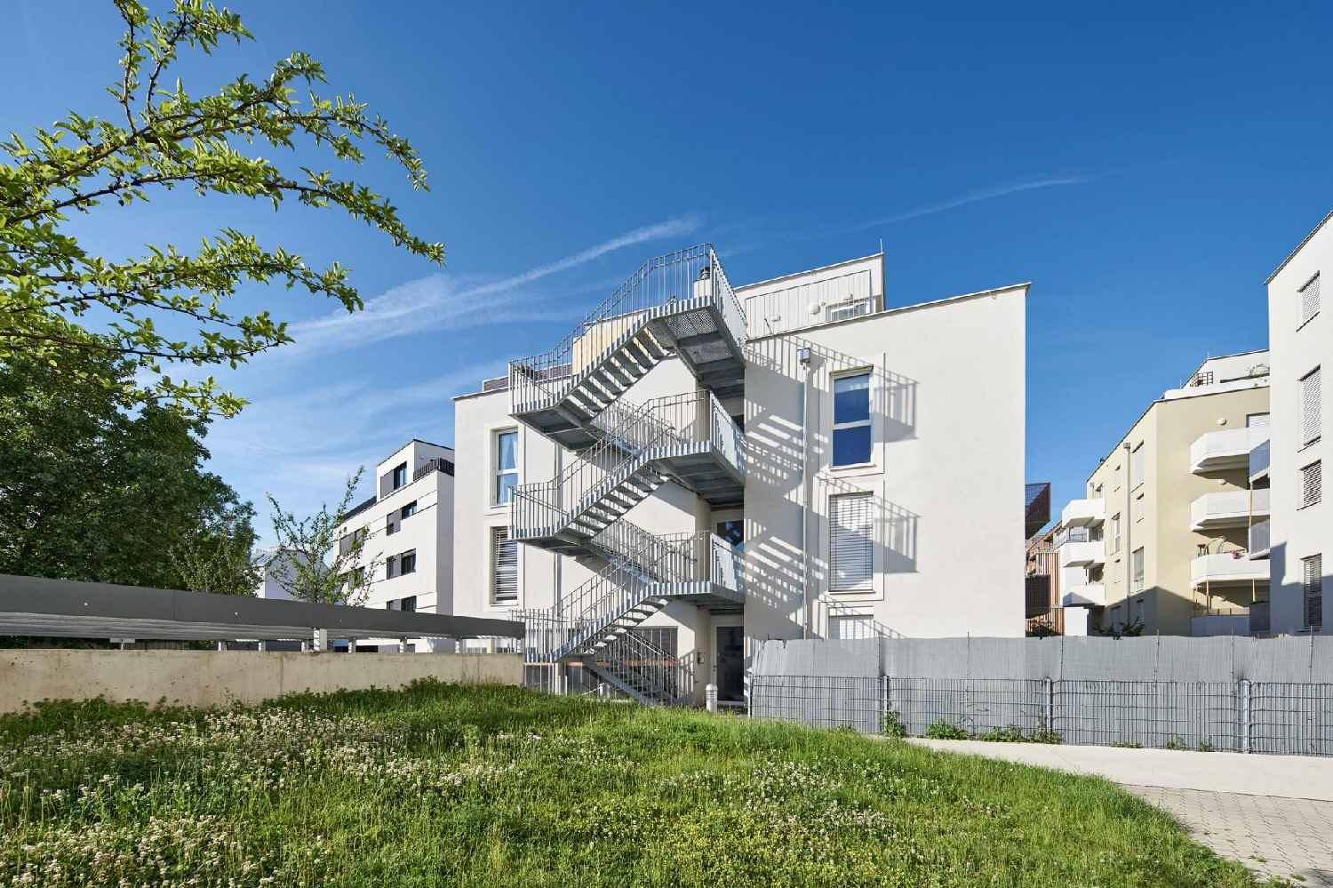 Moderne Gebäudefassade mit auffälliger Außentreppe und Grünfläche im Vordergrund.