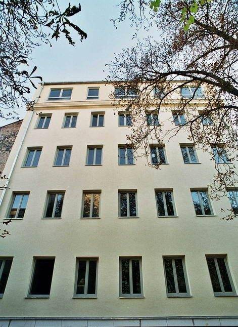 Rückfassade eines Gebäudes mit vielen Fenstern und schlichter Architektur, umgeben von Bäumen.