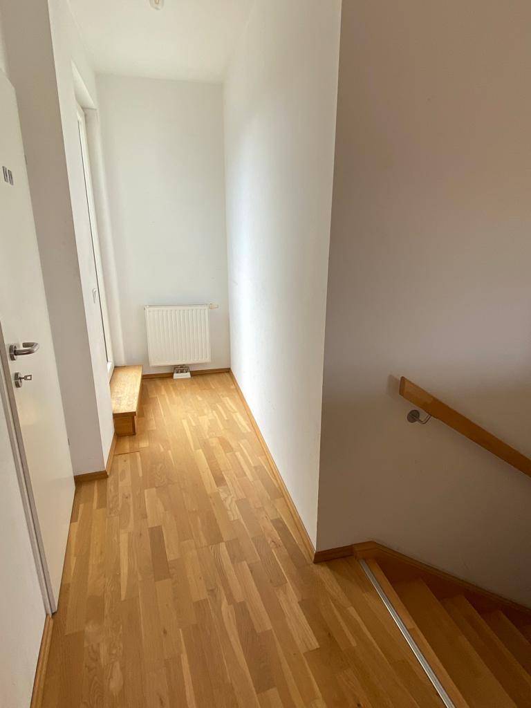 Heller Flur mit Parkettboden und Holztreppe, führt zu weiteren Bereichen der Wohnung.