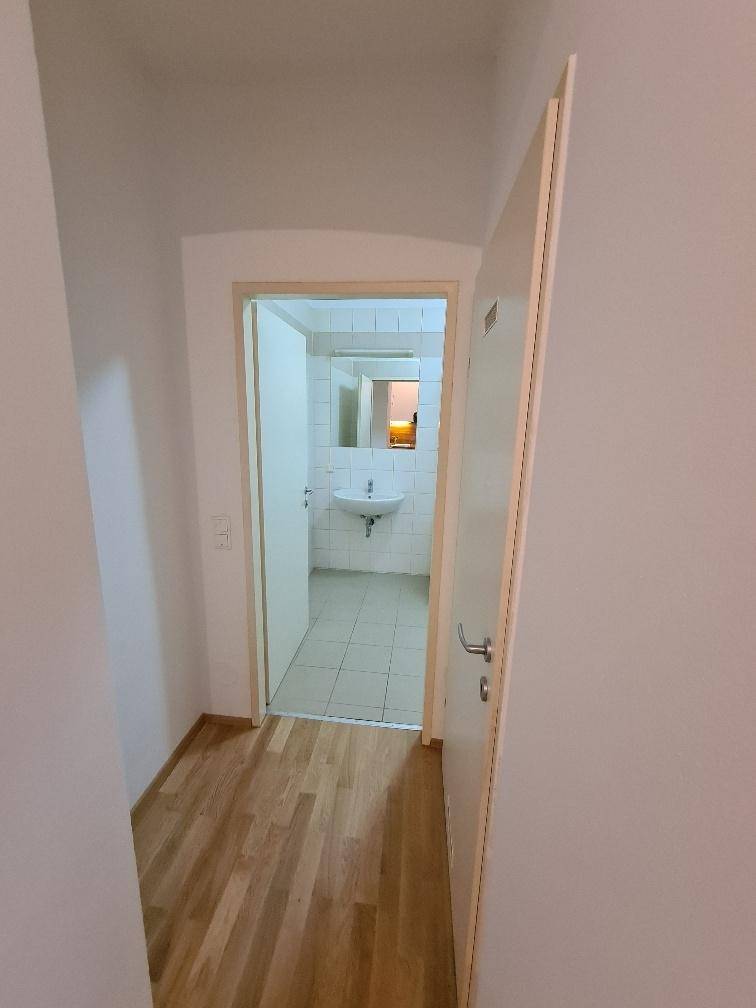 Heller Flur mit Parkettboden und offener Tür zu einem Badezimmer mit Waschbecken.