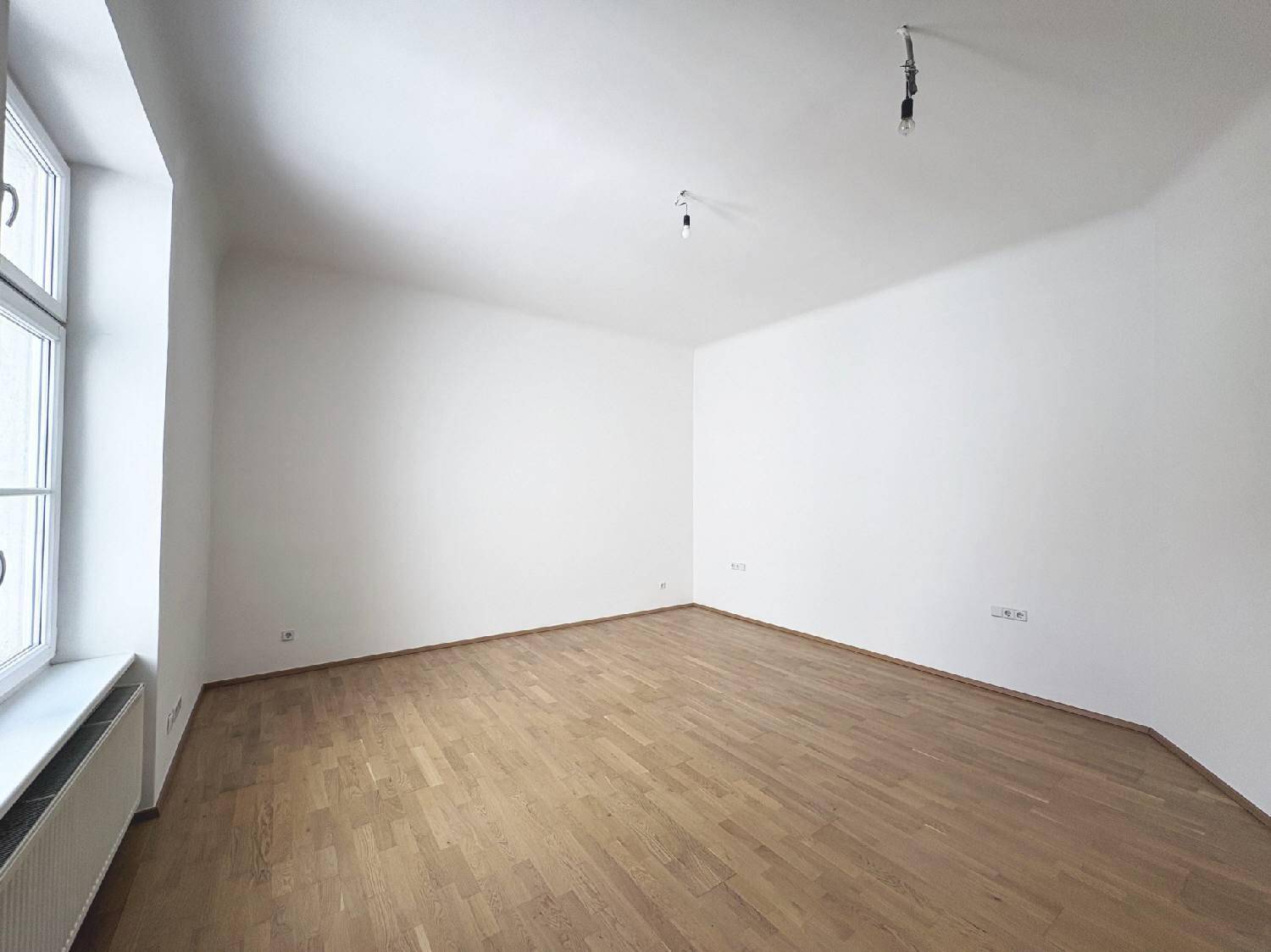 Geräumiges Zimmer mit hellem Parkettboden und viel Tageslicht, schafft eine angenehme Atmosphäre.