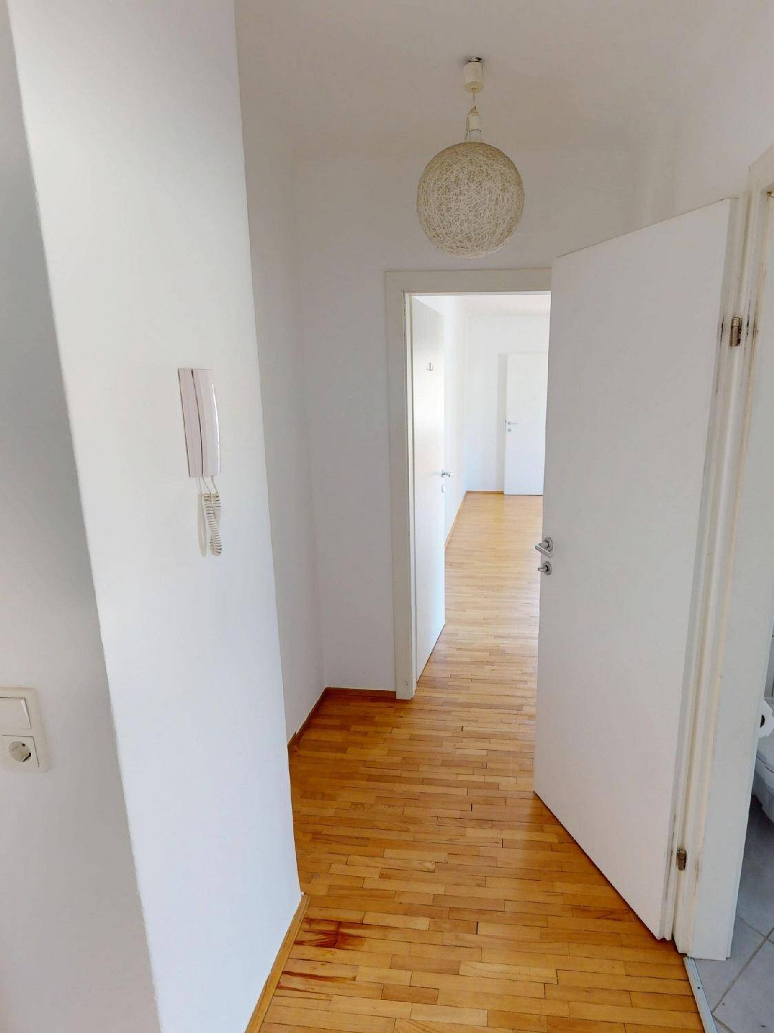Langer Flur mit Parkettboden und heller Beleuchtung, verbindet verschiedene Wohnbereiche.