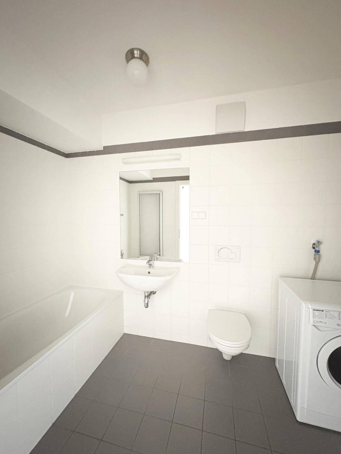 Funktionales Badezimmer mit Badewanne, WC, Waschbecken und Waschmaschine.