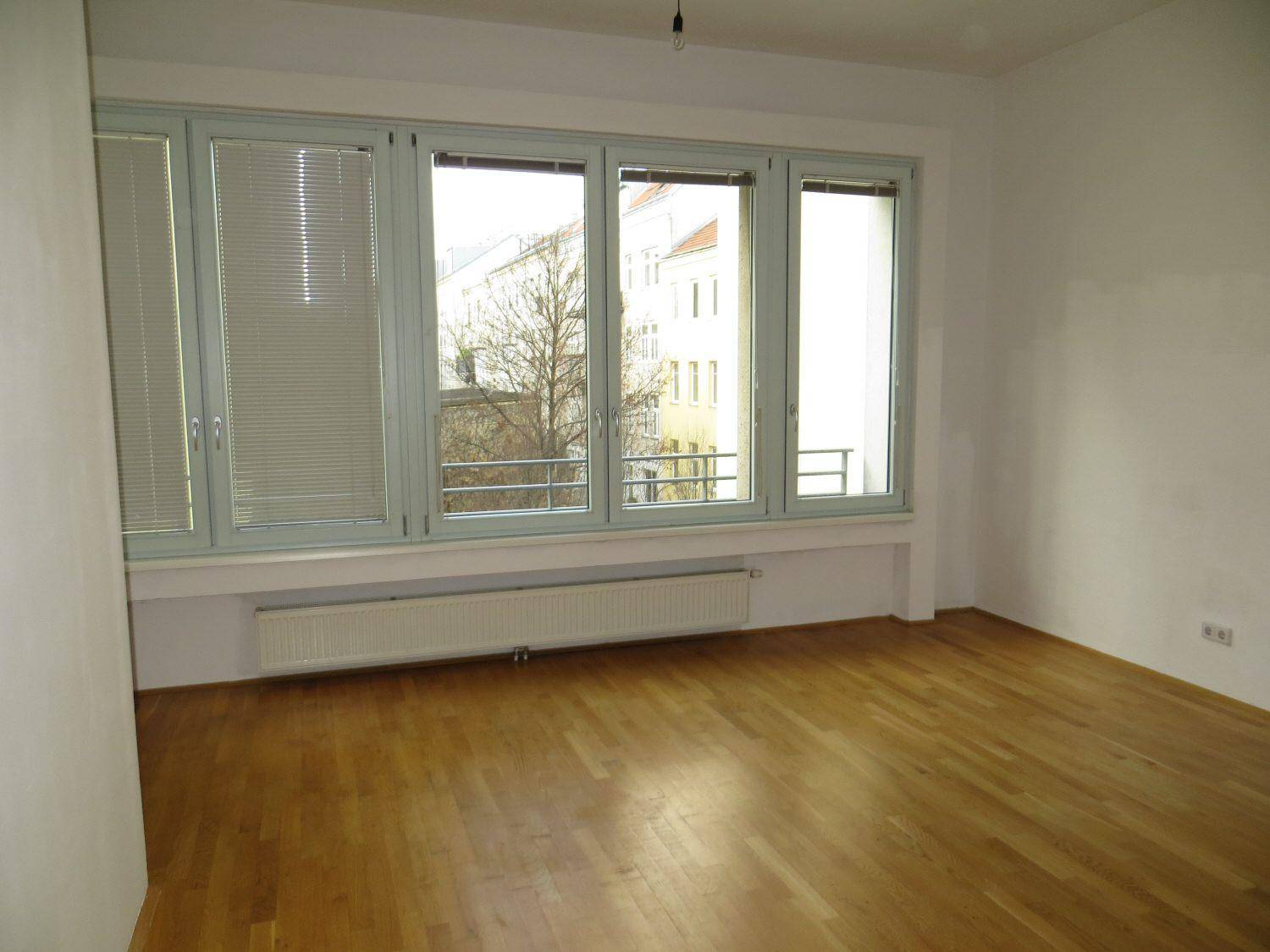 Leeres Zimmer mit hellem Parkettboden und breiten Fenstern, die eine angenehme Atmosphäre schaffen.