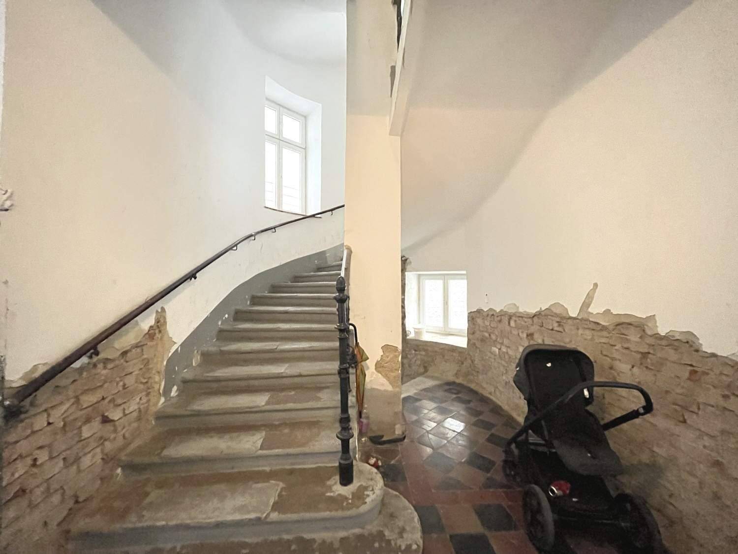 Altes Treppenhaus mit geschwungener Steintreppe, Geländer und sichtbaren Renovierungsspuren.